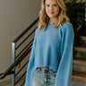 Close up view of model wearing the Love Always Sweater In Blue which features blue knit fabric, a cropped waist, a round neckline, dropped shoulders, and long sleeves with a relaxed fit.