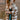 Close up view of model wearing the Twist Of Fate Cardigan which features brown and cream knit fabric, checkered pattern, tortoise button up front closure, v neckline, brown ribbed knit fabric outline and long balloon sleeves with brown ribbed knit wrists.