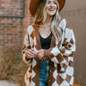 Close up view of model wearing the Twist Of Fate Cardigan which features brown and cream knit fabric, checkered pattern, tortoise button up front closure, v neckline, brown ribbed knit fabric outline and long balloon sleeves with brown ribbed knit wrists.