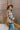Side view of model wearing the Twist Of Fate Cardigan which features brown and cream knit fabric, checkered pattern, tortoise button up front closure, v neckline, brown ribbed knit fabric outline and long balloon sleeves with brown ribbed knit wrists.