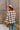 Back view of model wearing the Twist Of Fate Cardigan which features brown and cream knit fabric, checkered pattern, tortoise button up front closure, v neckline, brown ribbed knit fabric outline and long balloon sleeves with brown ribbed knit wrists.