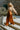 Side view of model wearing the Need More Time Satin Pants which features copper silk fabric, two front pockets, a zip and hook closure, a half elastic waistband, and wide legs.