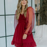 Close up view of model wearing the Fond Of You Dress which features burgundy fabric, smocked detailing with sweetheart neckline, ruffle hem, has a lining and organza long sleeves with elastic wrists.
