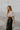 Side view of model wearing the My Eyes On You Bodysuit which features cream fabric, ruffle detailing, lettuce hem, square neckline, short puff sleeves with elastic band and thong bottom with button closures.