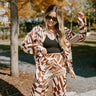 Close up view of model wearing the Follow Your Path Bottoms which features ivory and brown satin fabric with a geometric pattern, an elastic waistband, and wide legs.