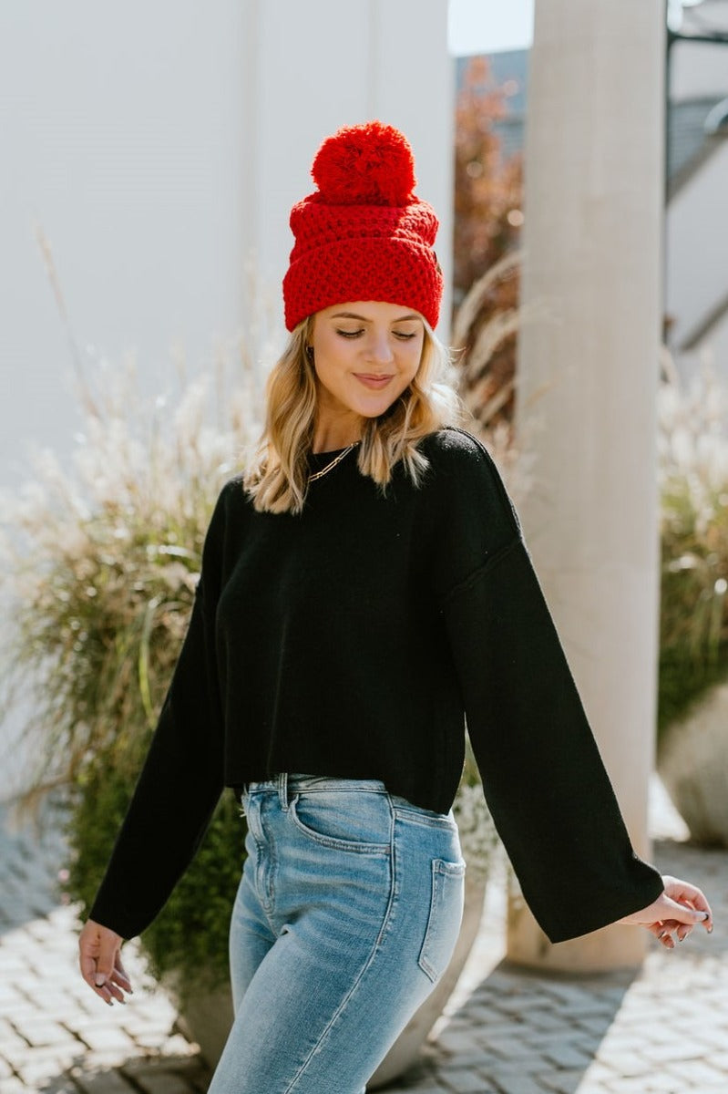 Front view of model wearing the Fireside Beanie in Pink that has pink knit fabric, a folded cuff with a brown "C.C" patch, and a pink pompom.
