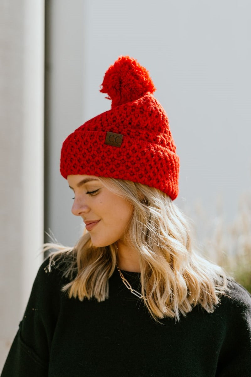 Close side view of model wearing the Fireside Beanie in Pink that has pink knit fabric, a folded cuff with a brown "C.C" patch, and a pink pompom.
