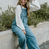 Back view of model wearing the One Way Ticket Overalls that feature dusty blue corduroy fabric, wide legs, one front pocket, two back pockets and button strap closures.