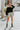 Full body front view of model wearing the Silver Lining Shorts that feature silver sheen fabric, an elastic smocked waistband, and a lining.