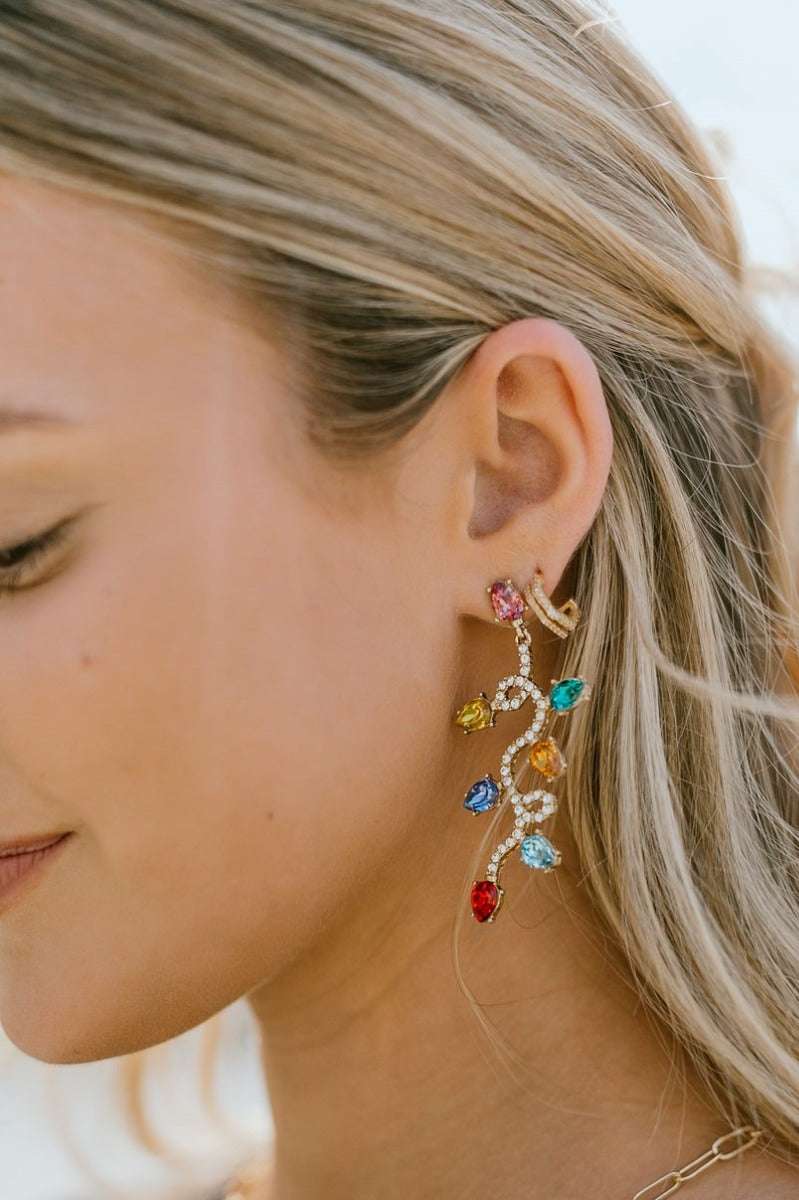 Close image of the model wearing the Light Up My World Earrings that feature a Christmas light design with multi-colored stones.