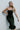 Front view of model wearing the The Big Dreams Midi Dress that has midi length black fabric, corset and ruched detailing, a feathered hem, s small slit in the back, a sleeveless body, and a lining.