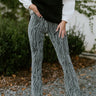 Front view of model wearing the Here For It Pants that feature black stretchy knit fabric with metallic silver stripes, an elastic waistband, and flare bottoms.