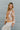 Side view of model wearing the Turn Back Time Top that has cream sheer fabric with mustard and brown pattern details, fabric covered buttons, a collared neckline, and long balloon sleeves with smocked wrists