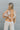 Back view of model wearing the Turn Back Time Top that has cream sheer fabric with mustard and brown pattern details, fabric covered buttons, a collared neckline, and long balloon sleeves with smocked wrists
