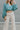 Close front view of model wearing the It Girl Pants that have natural color fabric, pleated details, two front pockets, a front zipper and hook closure, an elastic-back waistband with belt loops, and flare pant legs.