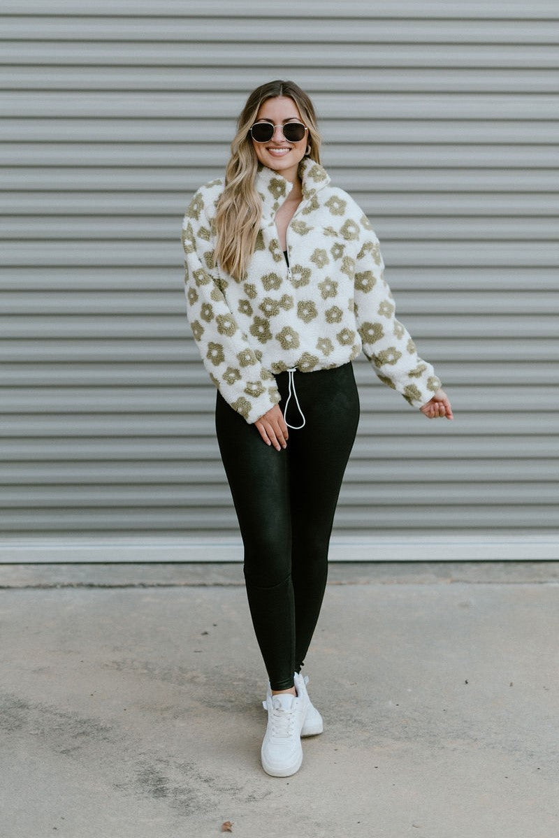 Full body front view of model wearing The In Bloom Teddy Jacket that has white teddy fabric with an olive flower pattern, a quarter zip closure with a collar, a cropped waist with a drawstring hem, and long sleeves.