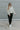 Full body front view of model wearing The In Bloom Teddy Jacket that has white teddy fabric with an olive flower pattern, a quarter zip closure with a collar, a cropped waist with a drawstring hem, and long sleeves.