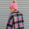 Side view of model wearing the Summit Beanie in Pink that features pink knit fabric, folded trim with a "C.C." emblem, and a faux fur pompom.
