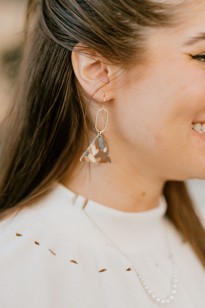 Close side view of model wearing the Empire State Of Mind Earrings that feature teal, burgundy, white and olive marbled triangle pendants connected to gold ovals.