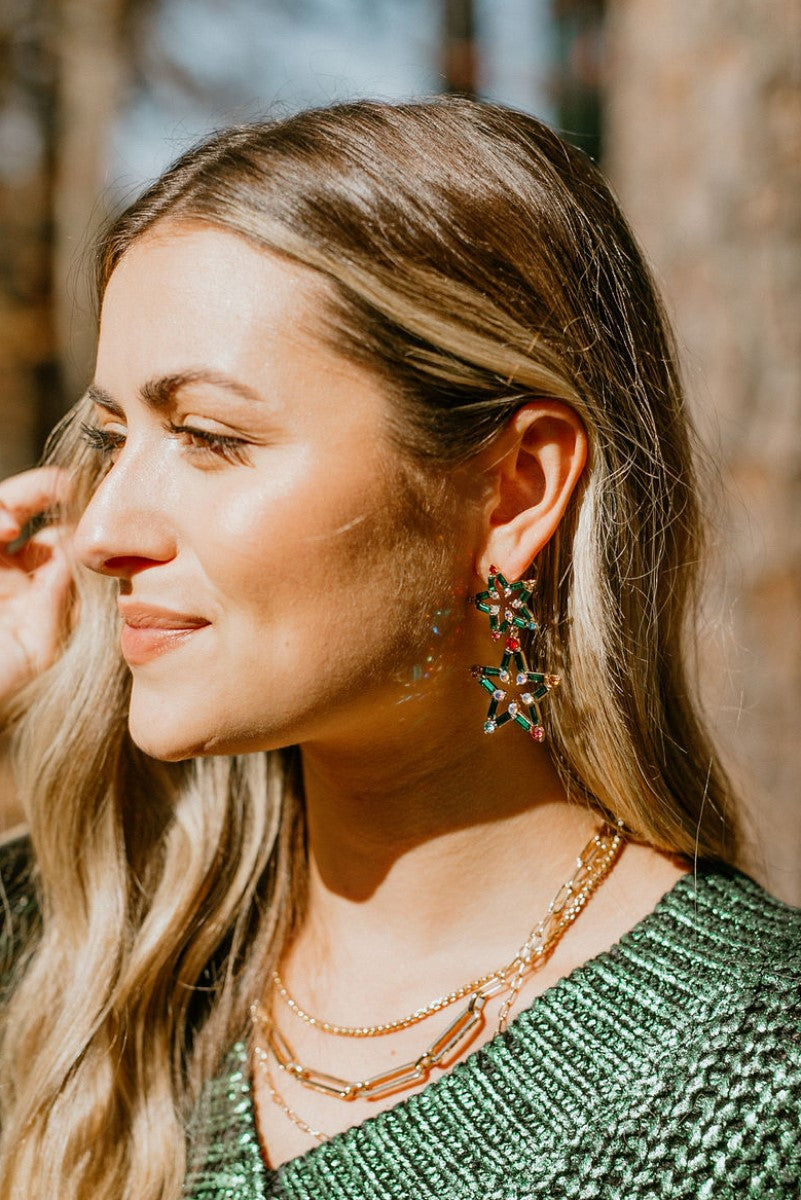 Side view of model wearing the Merry And Bright Earrings that feature star-shaped pendants with green and multi-colored stones.