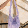 Front view of model holding the Ashley Bubble Tote Bag in Lilac which features lavender textured bubble fabric, one shoulder strap, lavender lining and monochrome zipper closure with silver hardware.