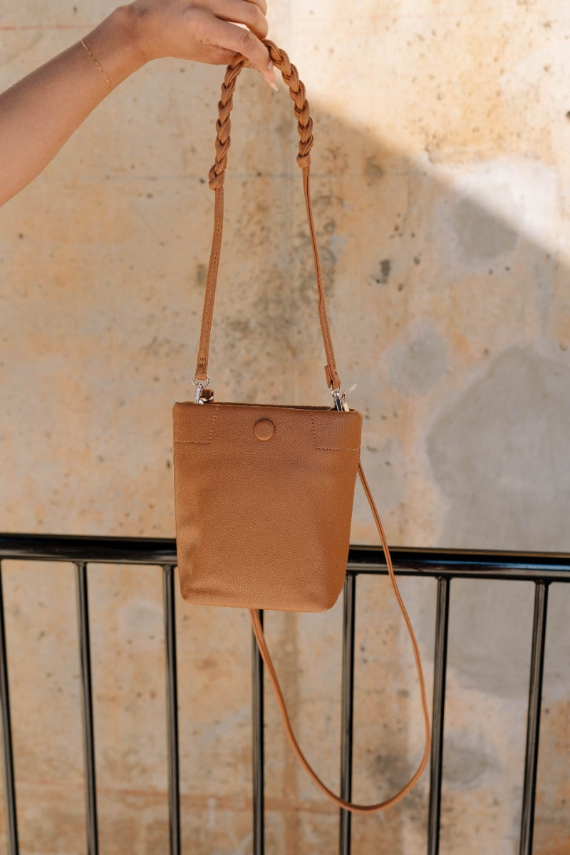 Front view of model holding the Trisha Brown Braided Straps Purse which features light brown faux leather fabric, two removeable shoulder straps, braided details and monochrome button snap closure.