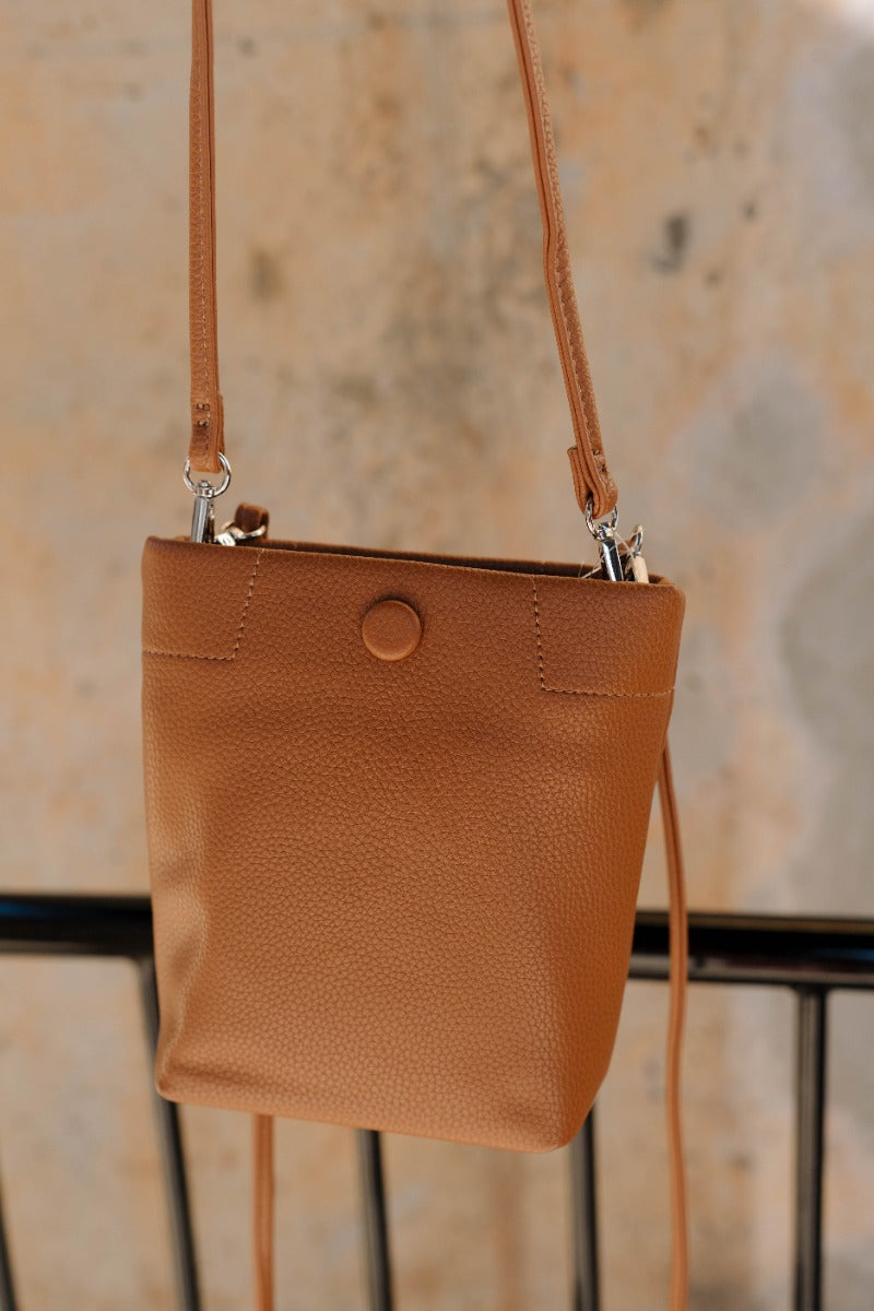 Close up view of model holding the Trisha Brown Braided Straps Purse which features light brown faux leather fabric, two removeable shoulder straps, braided details and monochrome button snap closure.