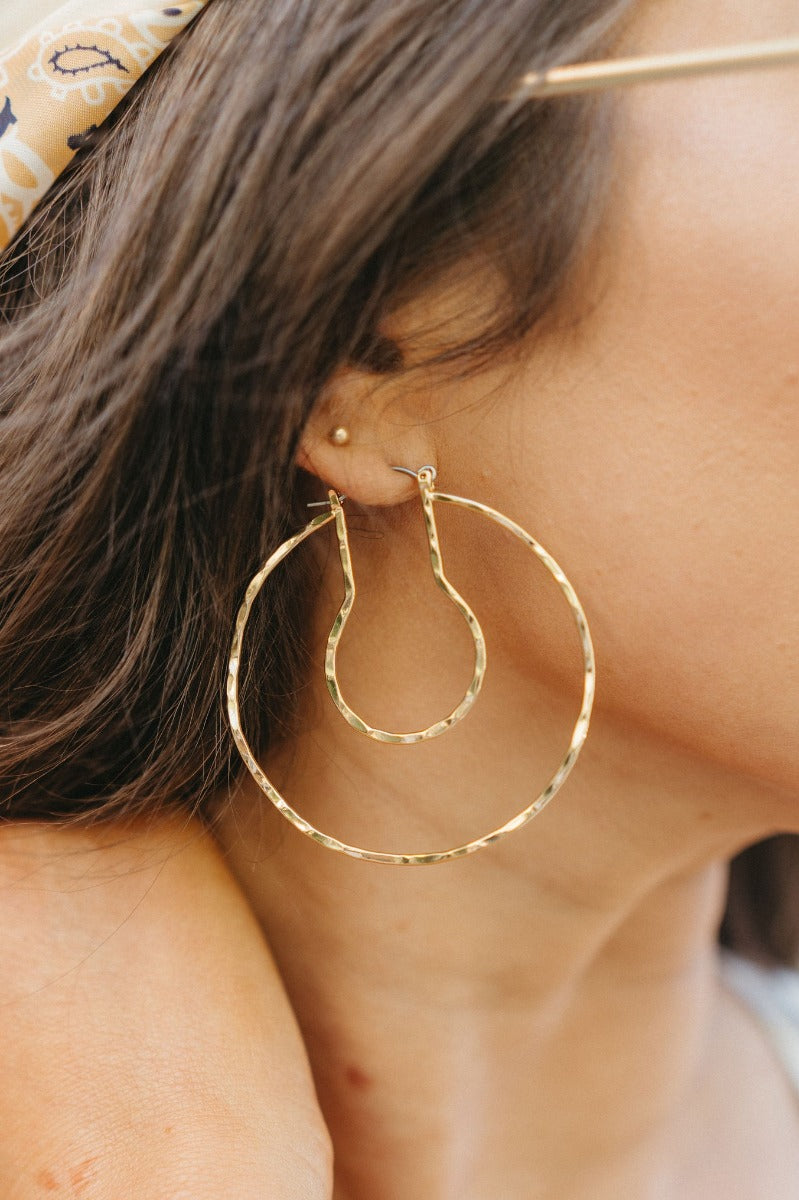 Close side view of model wearing the Hepburn Hoop Earring which features large closed hoop with gold hammered design.