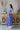 Side view of model wearing the Summertime Blues Maxi Dress that features royal blue fabric with a white floral print, maxi length, a slit on the side, a front tie closure, a surplice neckline and short sleeves