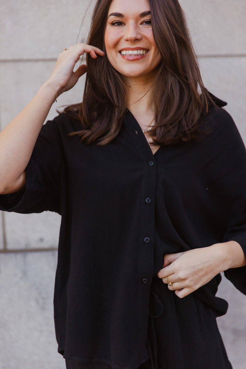 Front view of model wearing the Everleigh Black Button Up Short Sleeve Top which features black knit fabric, monochrome button up, collared neckline and short sleeves.