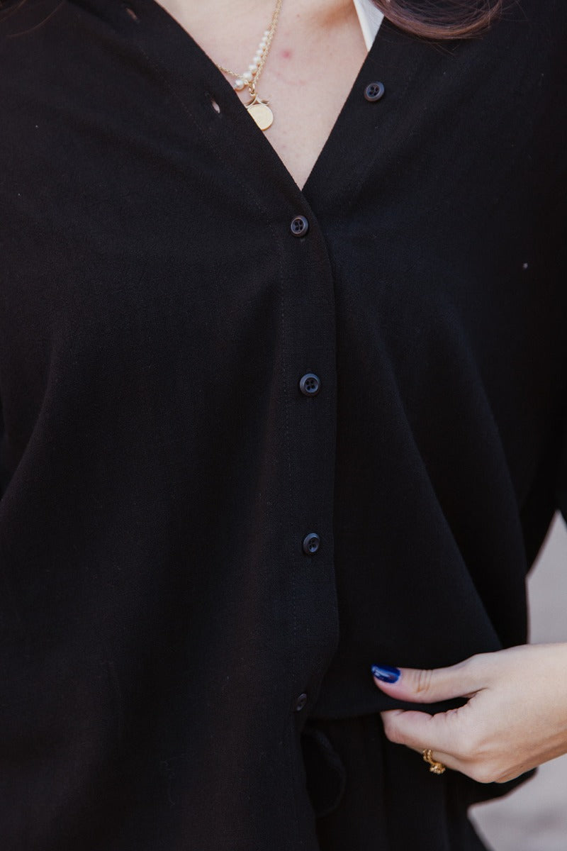 Close up view of model wearing the Everleigh Black Button Up Short Sleeve Top which features black knit fabric, monochrome button up, collared neckline and short sleeves.