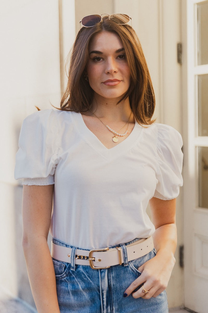 Front view of model wearing the Emma White Short Puff Sleeve Top which features white cotton fabric, a v-neckline, and short puff sleeves with smocked hem details.
