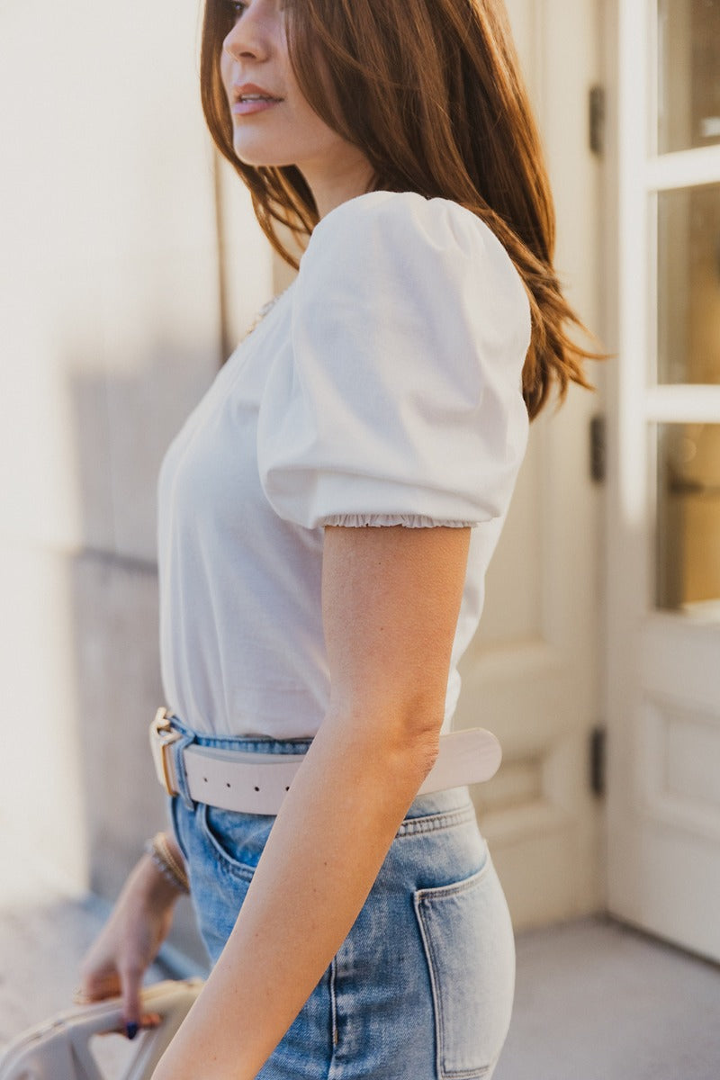 Side view of model wearing the Emma White Short Puff Sleeve Top which features white cotton fabric, a v-neckline, and short puff sleeves with smocked hem details.