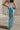 Back view of model wearing the Nova Aqua Blue Satin Midi Skirt which features turquoise satin fabric, maxi length, elastic band and monochrome side zipper with hook closure.