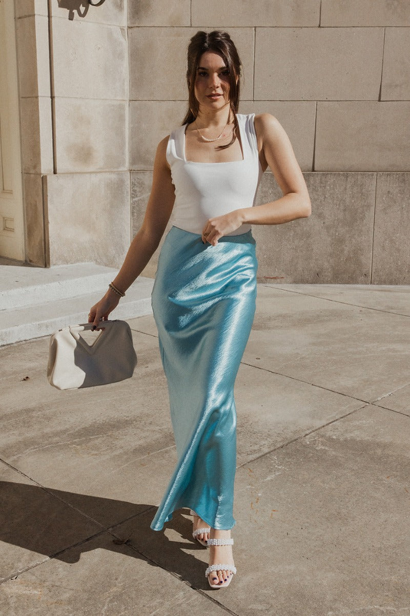 Full body view of model wearing the Nova Aqua Blue Satin Midi Skirt which features turquoise satin fabric, maxi length, elastic band and monochrome side zipper with hook closure.