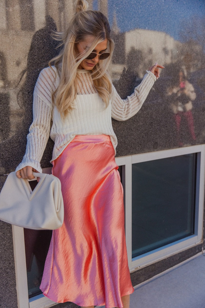 Front view of model wearing the Brooklyn Coral Satin Midi Skirt which features coral satin fabric, maxi length, elastic band and monochrome side zipper with hook closure.