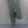 Front view of model wearing the Mia Grey Green Knit Pants which features gray green knit fabric, ribbed hem details, two front pockets, one back pockets, elastic waistband with drawstring ties and wide pant legs with drawstring ties at the ankles.
