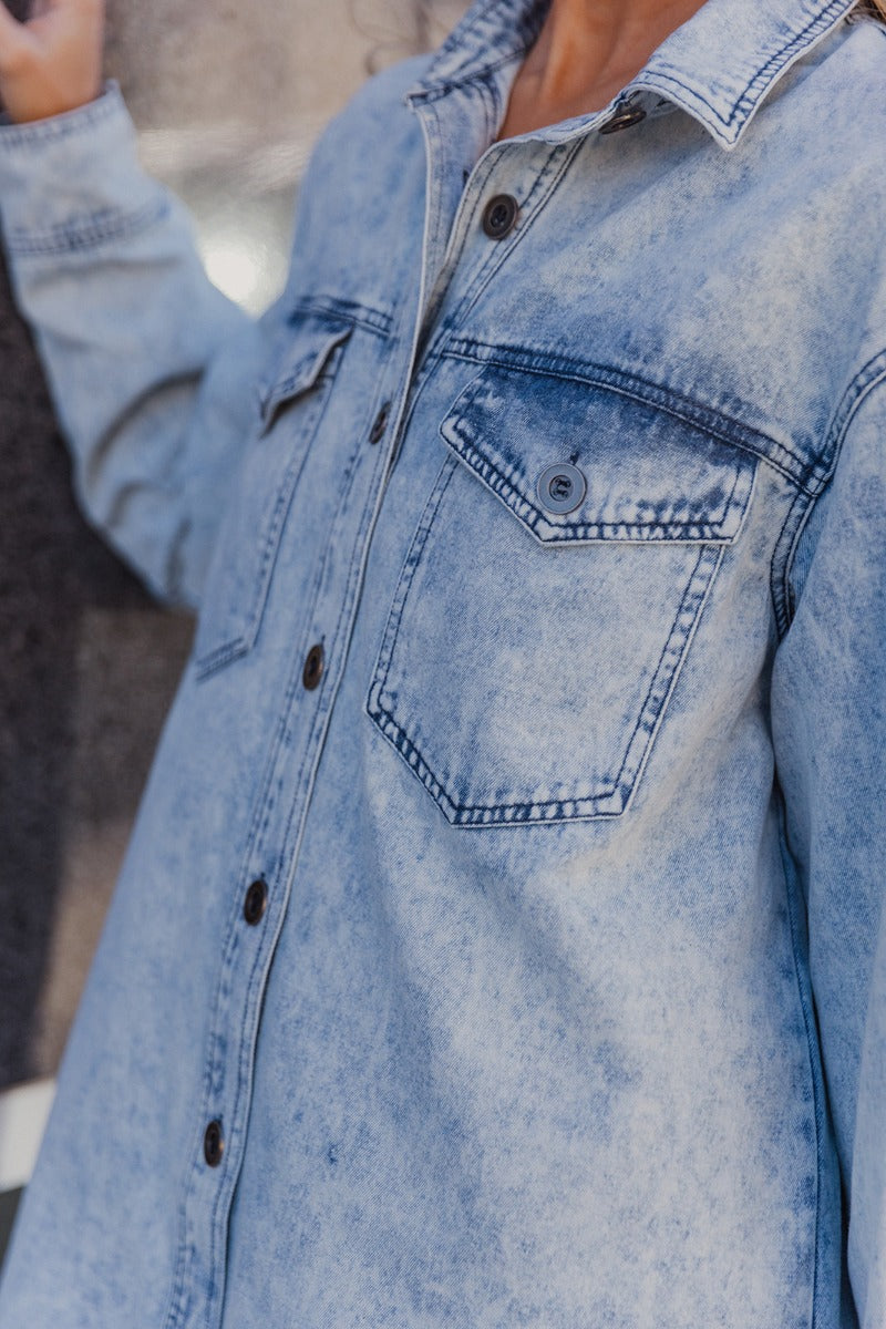 Close up view of model wearing the Jasmine Light Denim Wash Buttoned Long Sleeve Dress which features light wash denim fabric, button up closures, mini length, two front chest buttoned pockets, a collared neckline, and long sleeves with buttoned cuffs.