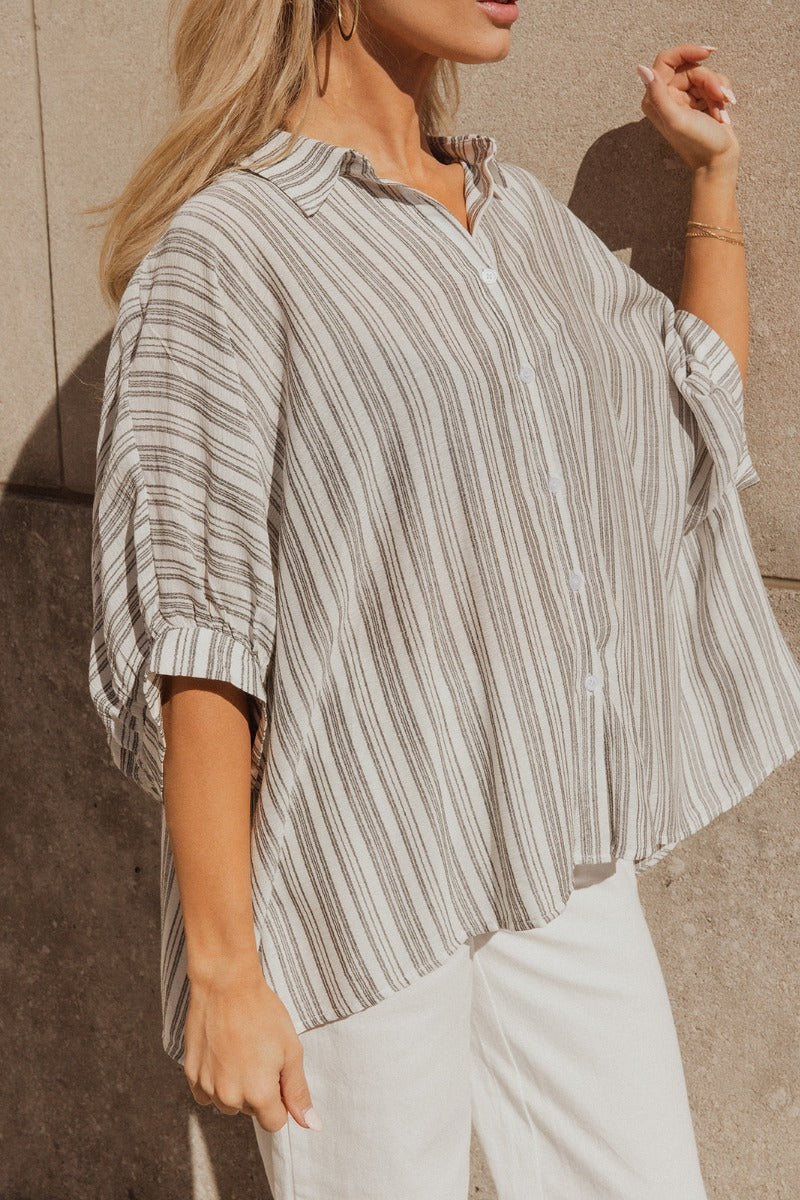 Close frontal/side view of model wearing the Sofia White & Black Striped Short Sleeve Top that has black and white rayon fabric with a striped pattern, clear button up closures, a collared neckline and short sleeves. 