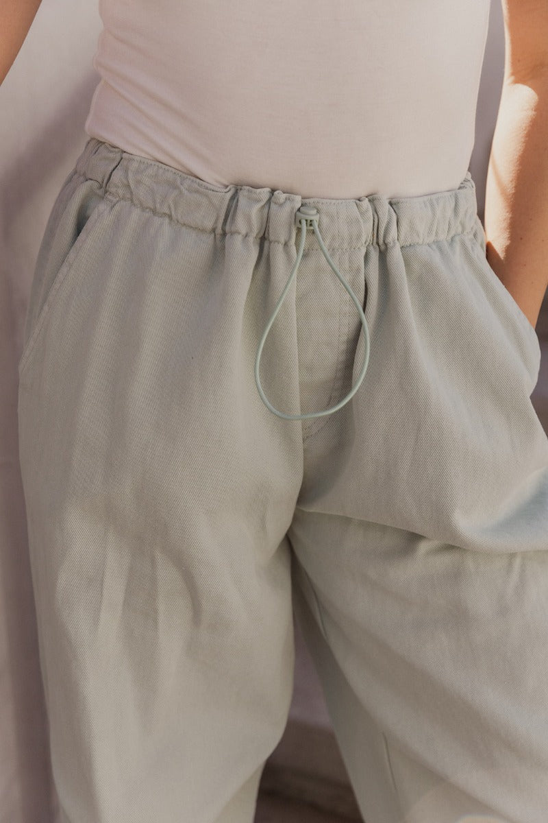 Close up view of model wearing the Cecilia Mint Green Pants which features mint denim fabric, two front slit pockets, two back pockets, elastic waistband with drawstring and wide pant legs with drawstrings at the ankles.