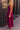 Full body side  view of model wearing the Valerie Magenta Sleeveless Ruffle Midi Dress which features magenta knit fabric, a ruffle hem, a front slit, a v neckline, adjustable spaghetti straps, and a monochromatic back zipper with a hook closure.