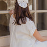 Back view of model's head while wearing the Camila Cream Satin Short Hair Bow that has short cream satin fabric shaped as a bow and a clasp closure.