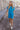 Full body front view of model wearing the Skylar Blue Short Sleeve Mini Dress that has ocean blue cotton fabric, mini length, two side pockets, a left chest pocket, a round neck, and short sleeves with folded hems.