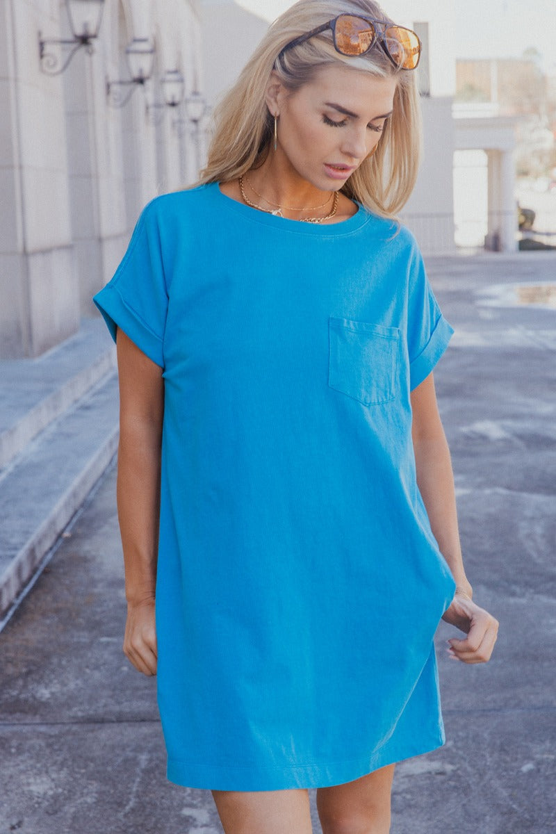 Front view of model wearing the Skylar Blue Short Sleeve Mini Dress that has ocean blue cotton fabric, mini length, two side pockets, a left chest pocket, a round neck, and short sleeves with folded hems.