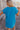 Back view of model wearing the Skylar Blue Short Sleeve Mini Dress that has ocean blue cotton fabric, mini length, two side pockets, a left chest pocket, a round neck, and short sleeves with folded hems.
