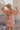Back view of model wearing the Eloise Multi-Color Swirl Print Mini Dress that has blush, orange, peach, pink, beige, rust and sage fabric, a swirl pattern, two tiered body, mini length, a v-neck, a smocked back and half sleeves with elastic trim.
