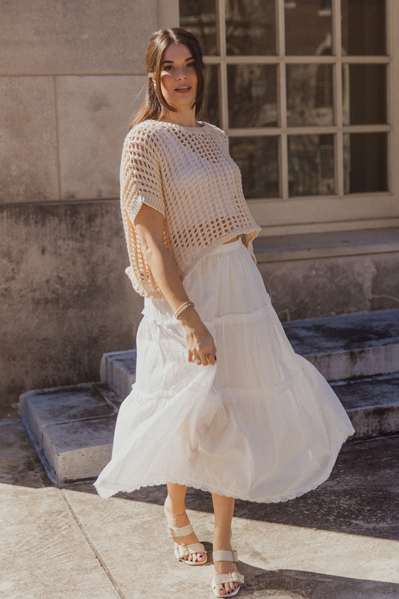 Full body front view of model wearing the Athena White Tiered Maxi Skirt that features white lightweight fabric, a two tiered body with ruffle details, a lace hem, midi length, white lining, and an elastic waistband.