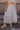 front view of model wearing the Athena White Tiered Maxi Skirt that features white lightweight fabric, a two tiered body with ruffle details, a lace hem, midi length, white lining, and an elastic waistband.