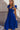 Frontal side view of model wearing the Kristina Royal Blue Smocked Sleeveless Midi Dress that has royal blue fabric, side slit pockets, midi length, smocked upper, a scoop neckline, and ruffled straps.