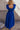 Back view of model wearing the Kristina Royal Blue Smocked Sleeveless Midi Dress that has royal blue fabric, side slit pockets, midi length, smocked upper, a scoop neckline, and ruffled straps.